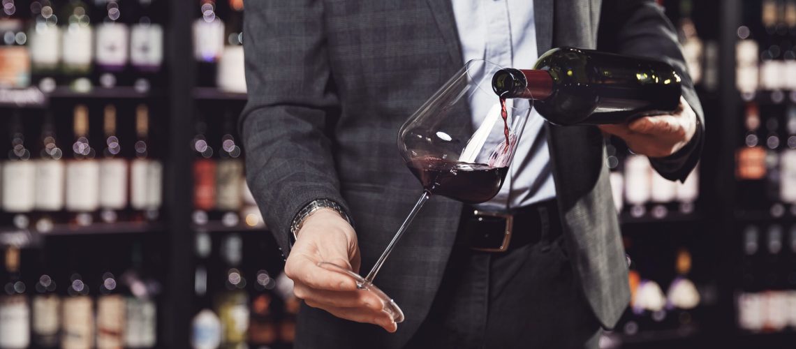 Banner sommelier pours wine into elegant glass goblet from bottle